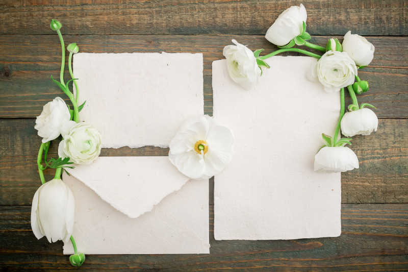 纸明信片信封和白色的花在木制的背景上