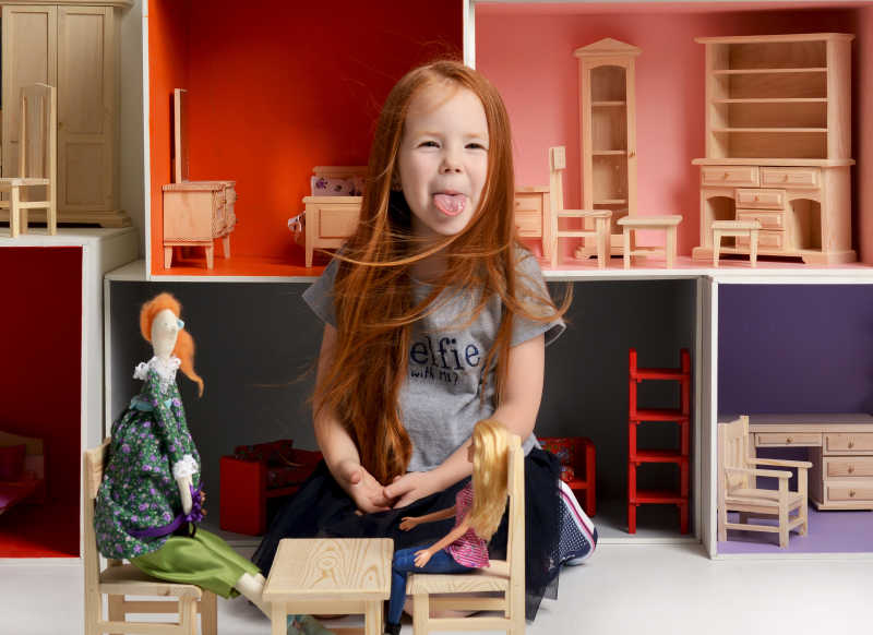 调皮吐舌头的小女孩玩小型桌椅和娃娃