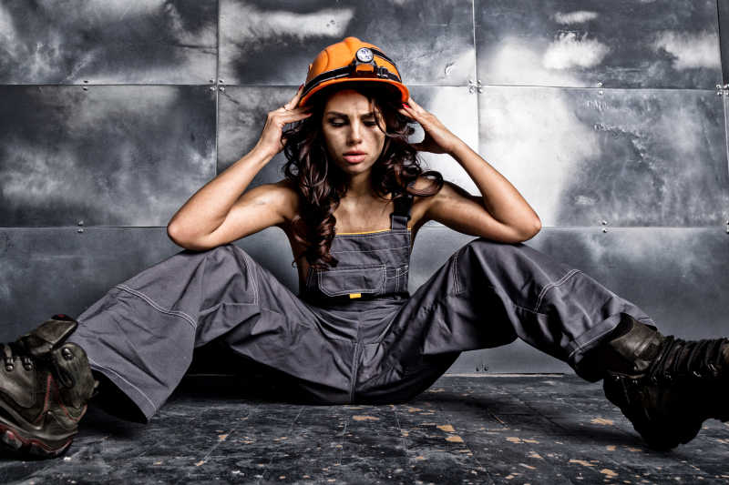 坐在地上双手拿着安全帽的年轻女矿工