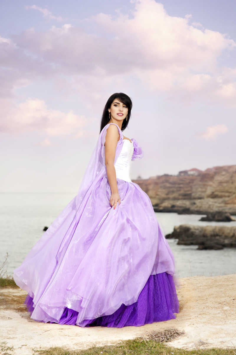 美丽苗条的新娘穿着紫色婚纱礼服站在海边