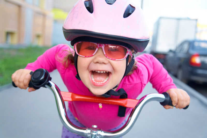 骑在自行车上的粉红色安全头盔的快乐小女孩