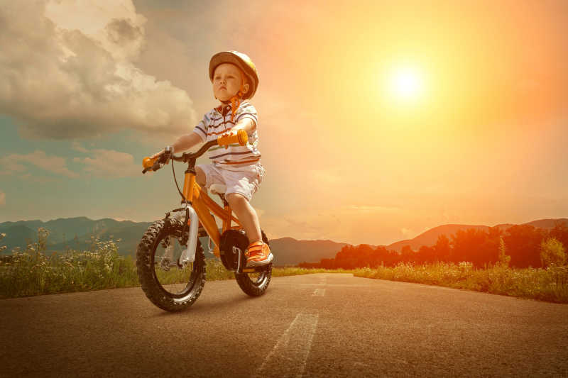 坐在橙色自行车上的儿童在非城市道路上骑行