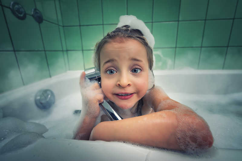 趴在浴缸里用淋浴头假装打电话的创意女孩特写