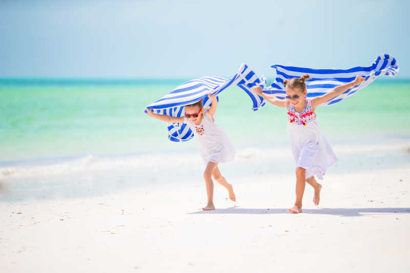在热带海滩上用毛巾跑步的两个小女孩