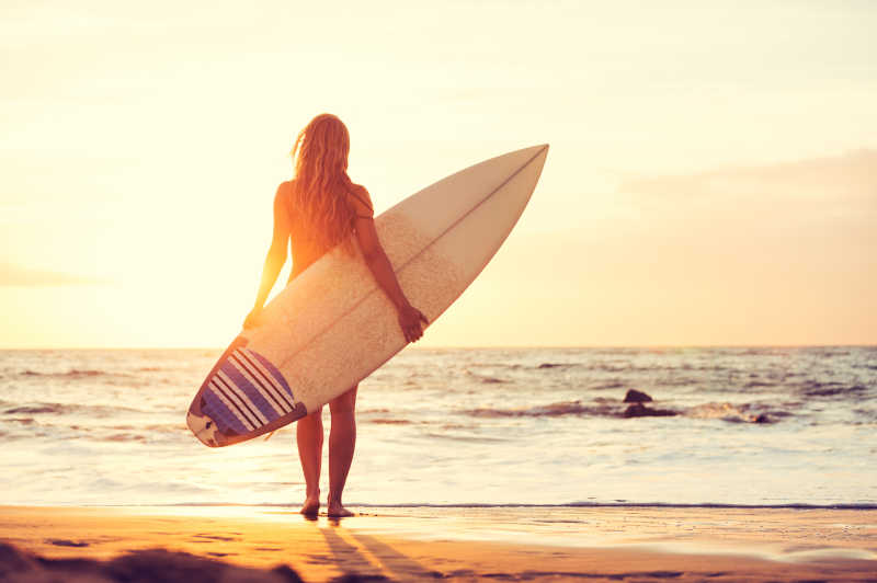 日落时分在海滩上冲浪的女孩