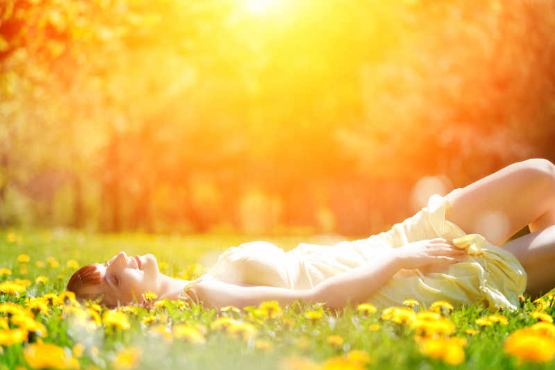 女人惬意的躺在阳光下的草地上