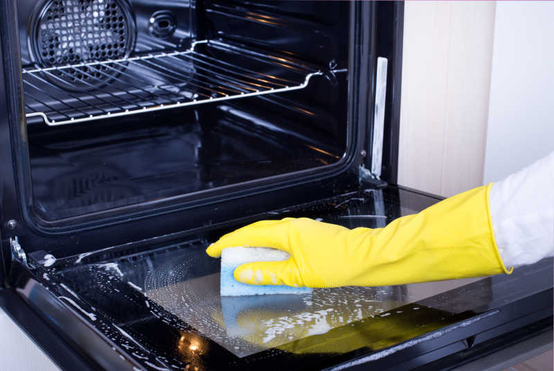 戴着黄色保护手套清洁烤箱炉门