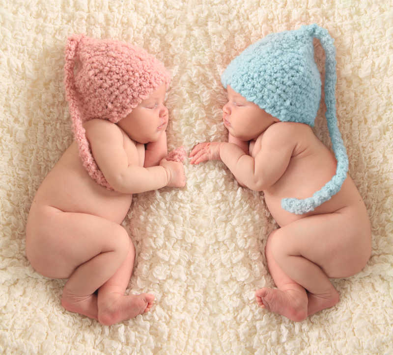 戴着不同颜色帽子睡着了的双胞胎宝宝