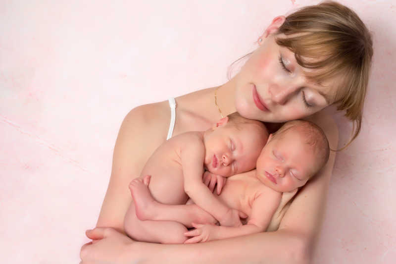 粉色背景下年轻的妈妈抱着双胞胎宝宝