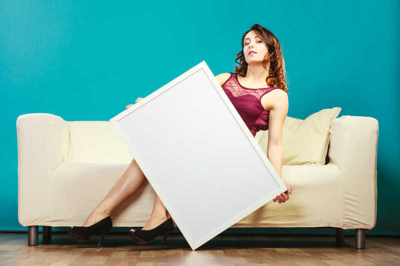 优雅的年轻女子坐在沙发上拿着空白的展示板