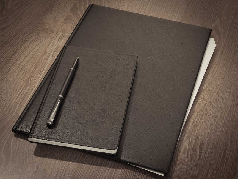 木制桌面上的黑色笔记本和笔