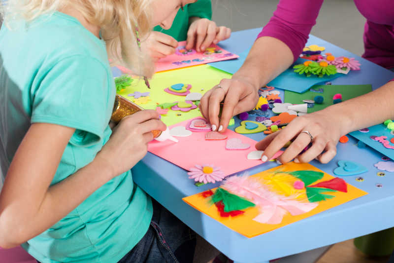 小女孩正在跟老师学习在彩色纸上做装饰品