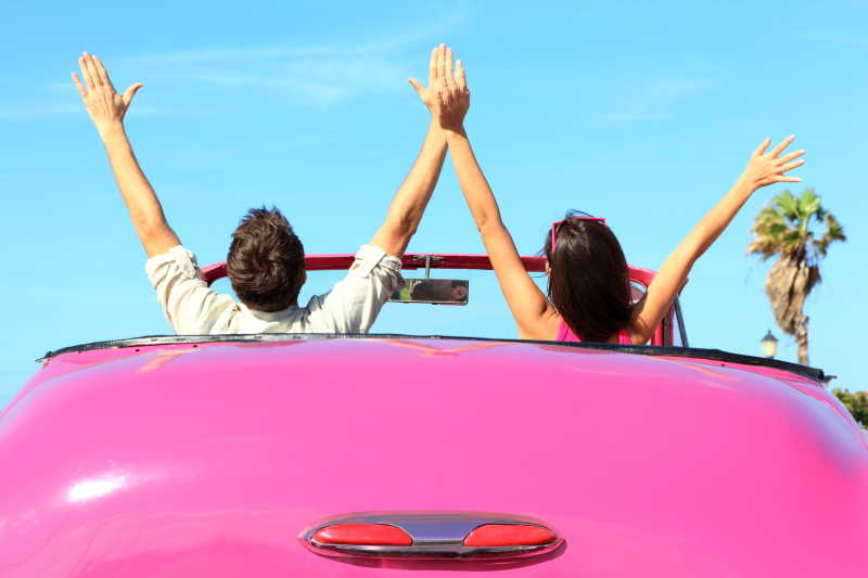 自由快乐的情侣驾驶粉红色复古汽车欢呼喜悦举起手臂
