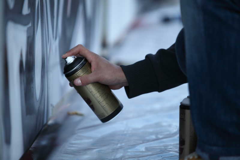 一个人拿着涂鸦罐在黑灰色的墙上喷画