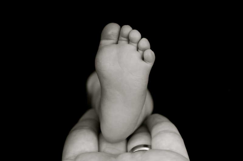 黑色背景下婴儿的脚放在大人的手上