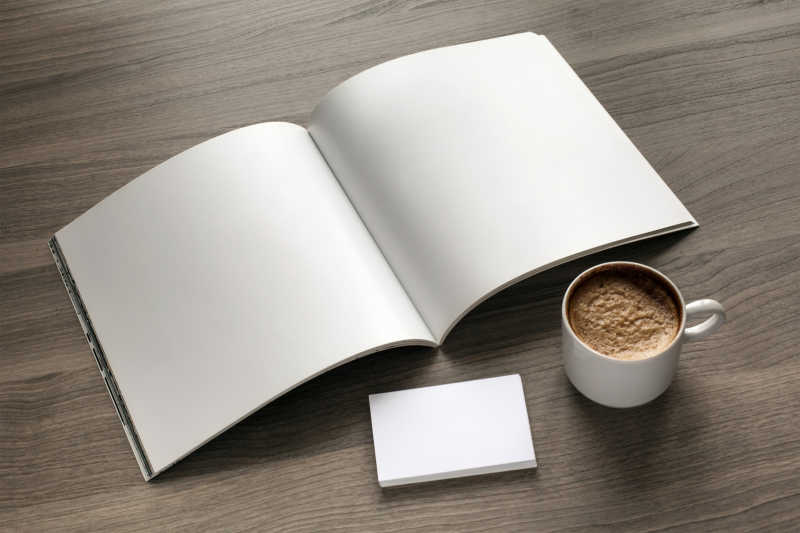 木质桌面上打开的白色日记本和一杯咖啡