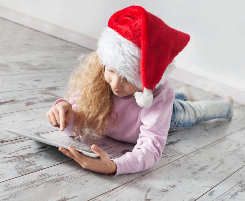 戴圣诞帽的小女孩在玩平板电脑