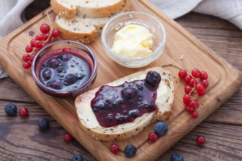 木头桌子上的蓝莓和红醋栗果酱黄油面包