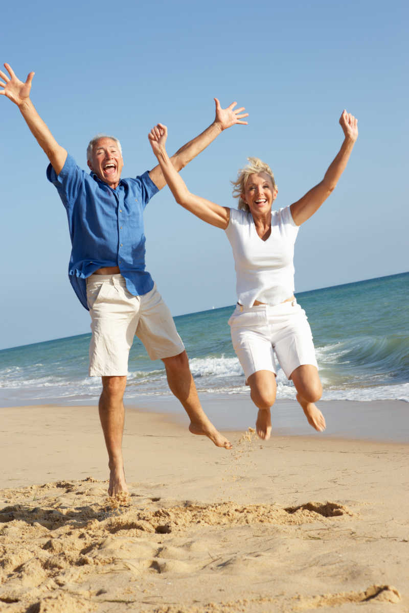 老年夫妇享受海滩假日在空中跳跃