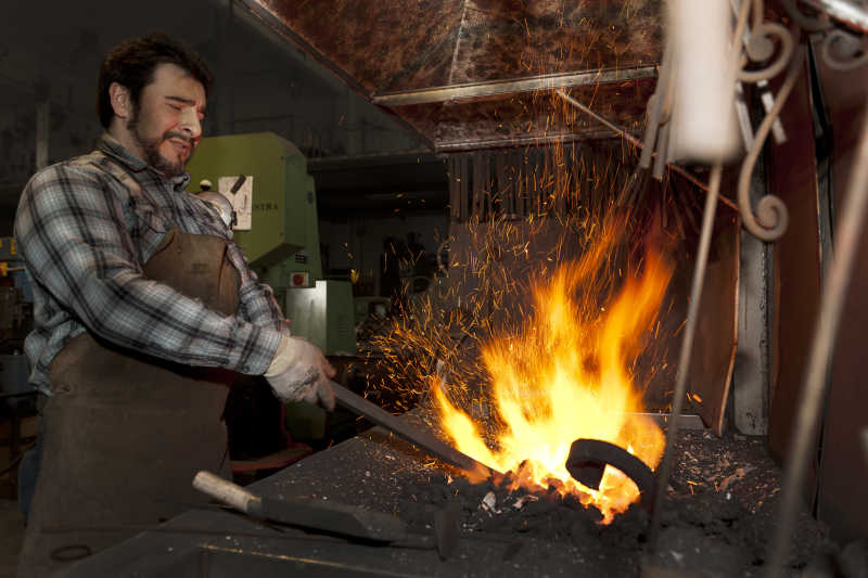 铁匠用钳子捏着金属在炉火中燃烧