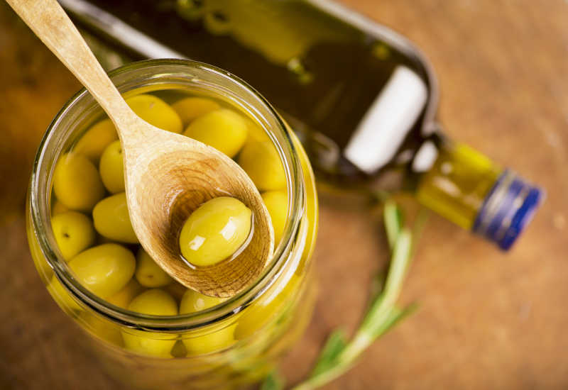 木色桌面上玻璃瓶里带有橄榄油的橄榄果