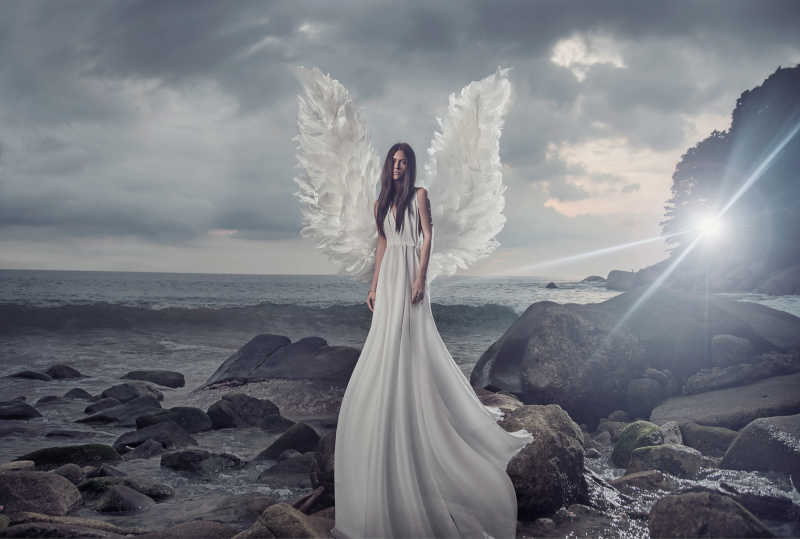 站在岩石上戴着天使翅膀白色礼服的美女