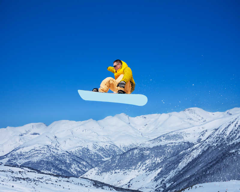 酷帅的滑雪男子拿着滑雪板在山的背景跳跃的空气