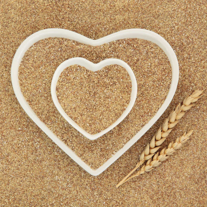 小麦胚芽的心脏形的白色瓷碟与小麦叶鞘形成背景