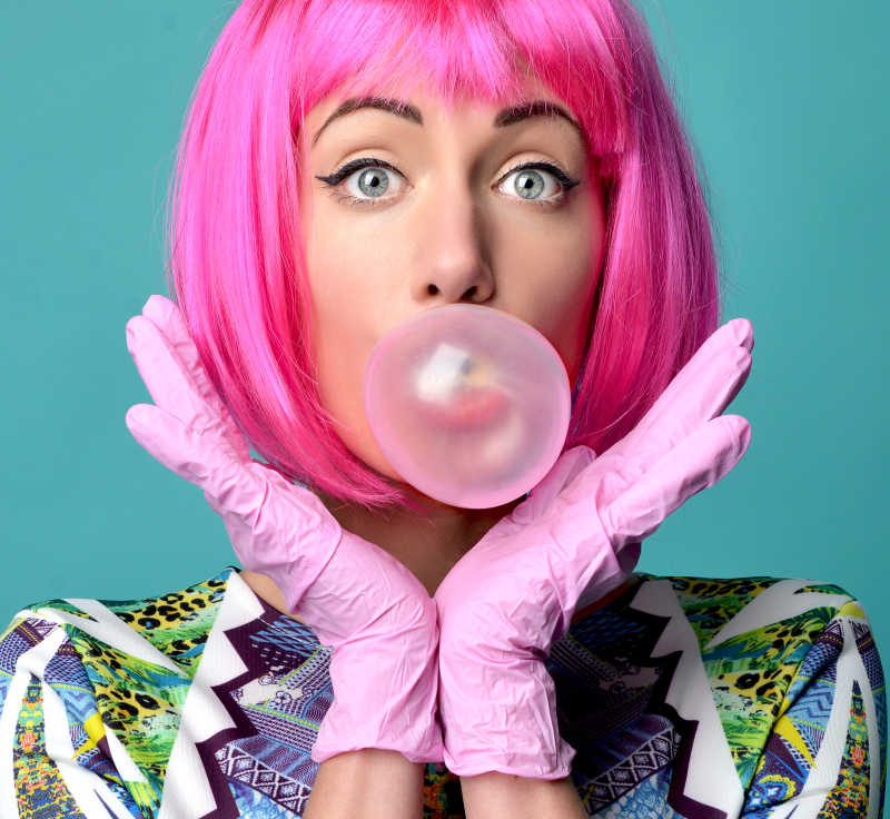 薄荷绿色背景下戴着粉色假发粉色手套的女人吹泡泡糖