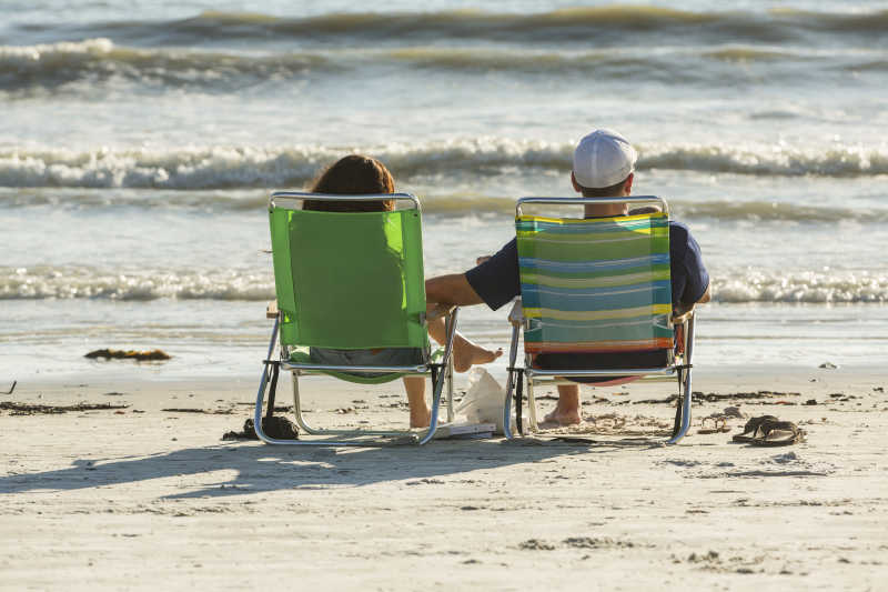 在海滩上坐着休闲椅的两个人