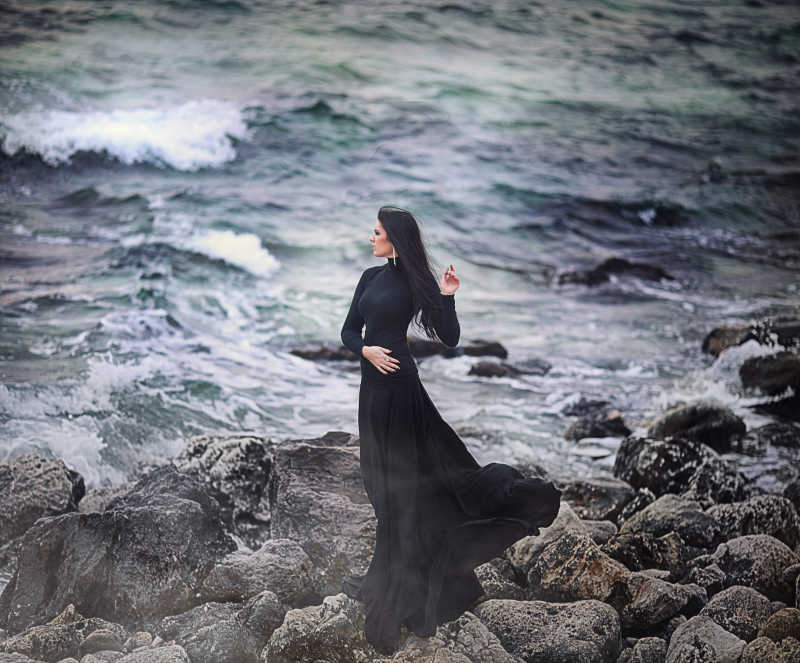 海边岩石上穿黑色长裙的时尚女士