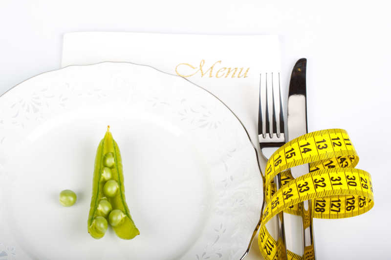 白色背景下盘子上的豌豆以及测量卷尺和刀叉