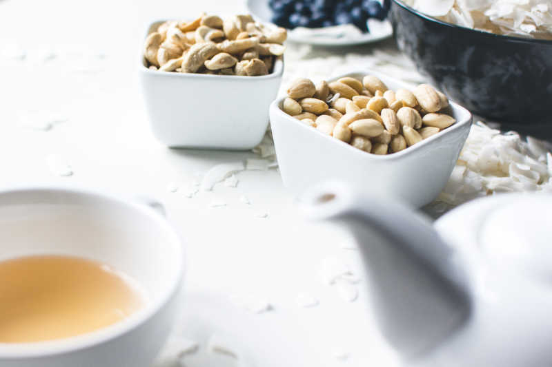 白色桌面上的碗装腰果和茶水