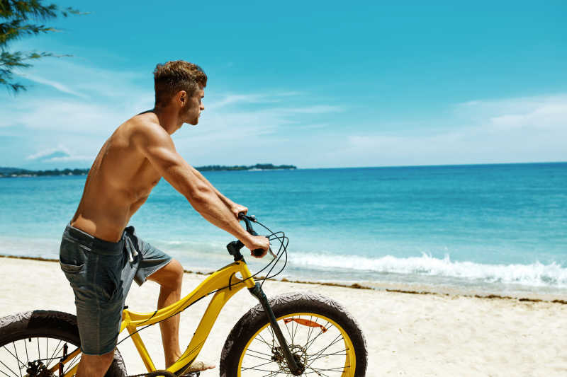 夏日沙滩有肌肉的帅哥骑着黄色沙滩自行车