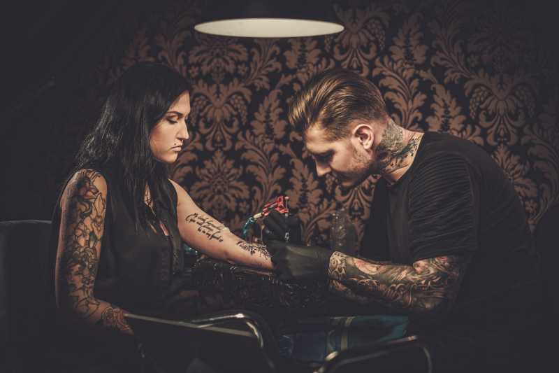 纹身师在年轻女孩的手臂上做纹身