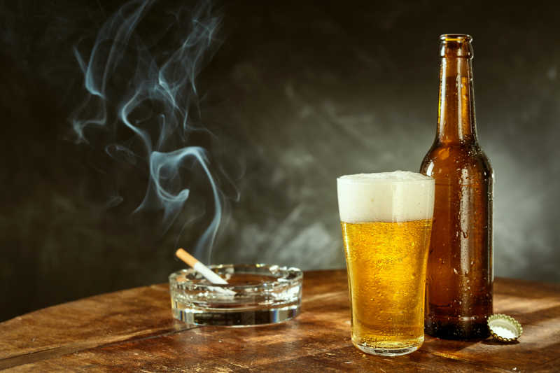 木桌上的啤酒和燃烧的香烟
