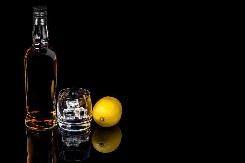 瓶和玻璃威士忌与冰和柠檬在黑色背景