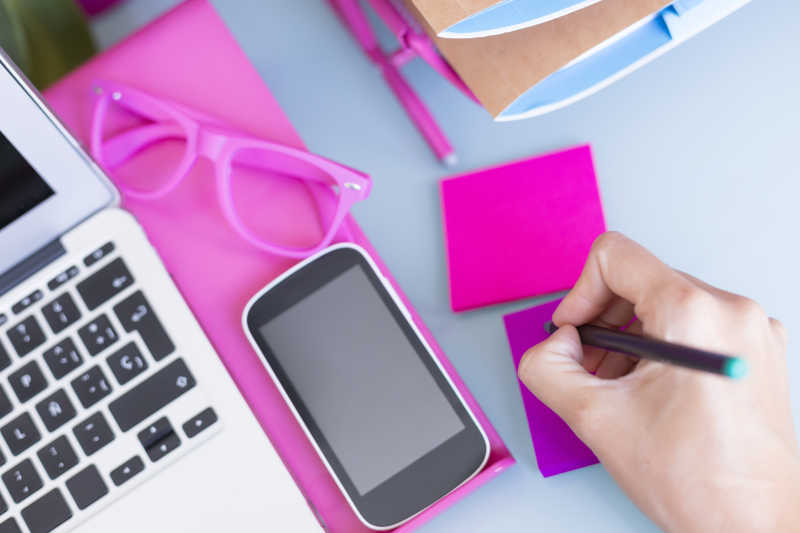 使用手机和笔记本旁边粉色便签的女人