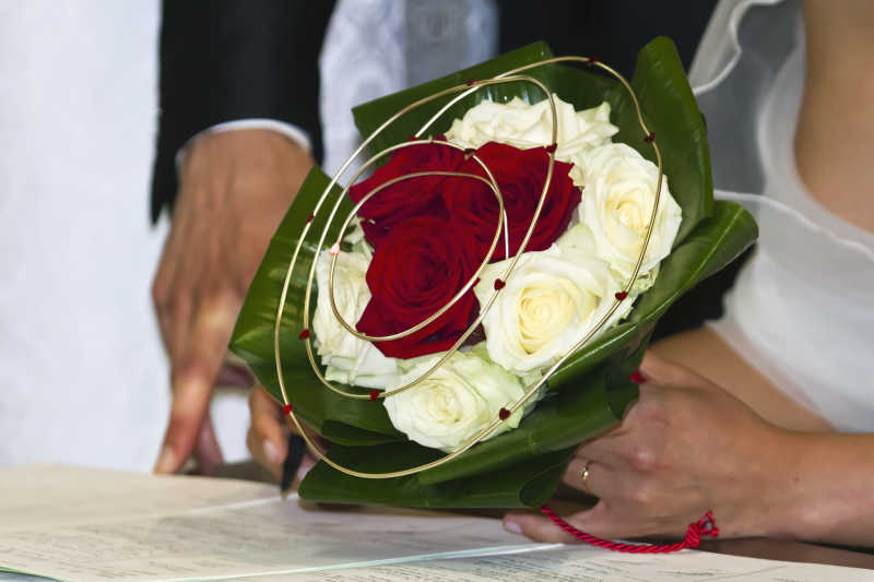 捧着白玫瑰和红玫瑰花束的新娘和新郎