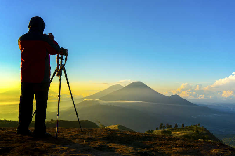 站在高山上拍摄日出风景的摄影师
