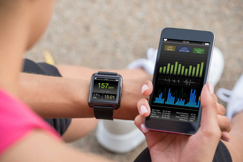 女跑步者看着她的手机和智能手表心率监视器