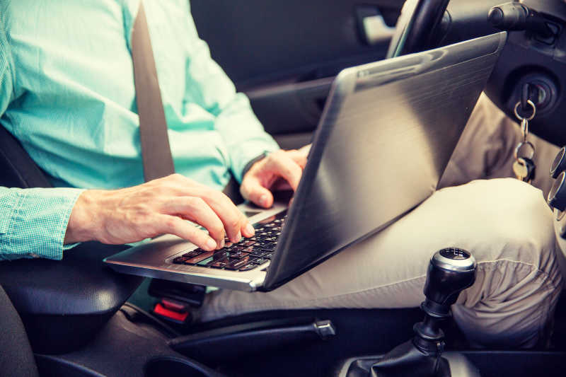 年轻人用笔记本电脑驾驶汽车的靠拢
