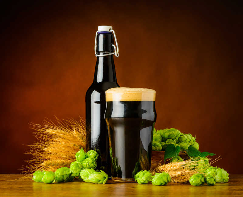 褐色背景下木桌上的一瓶黑啤酒和麦穗