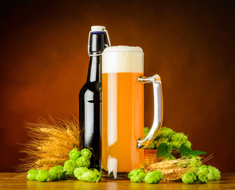 褐色背景下木桌上的一些小麦穗一瓶啤酒和一杯啤酒