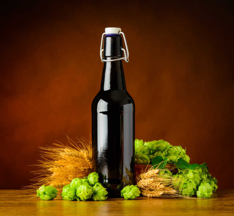 褐色背景下木桌上的一瓶啤酒和一些小麦穗
