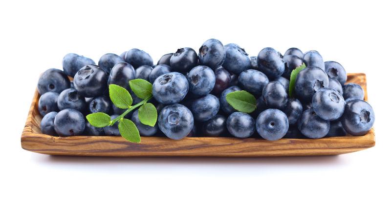 木盘里新鲜带绿叶的蓝莓