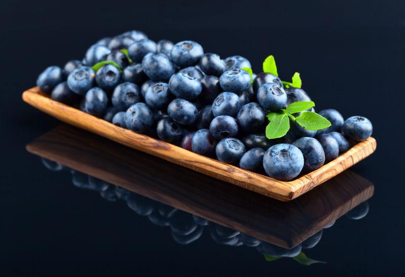 黑色背景下木盘中的新鲜蓝莓