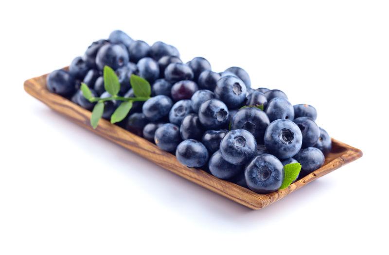 白色背景下木盘里的新鲜蓝莓