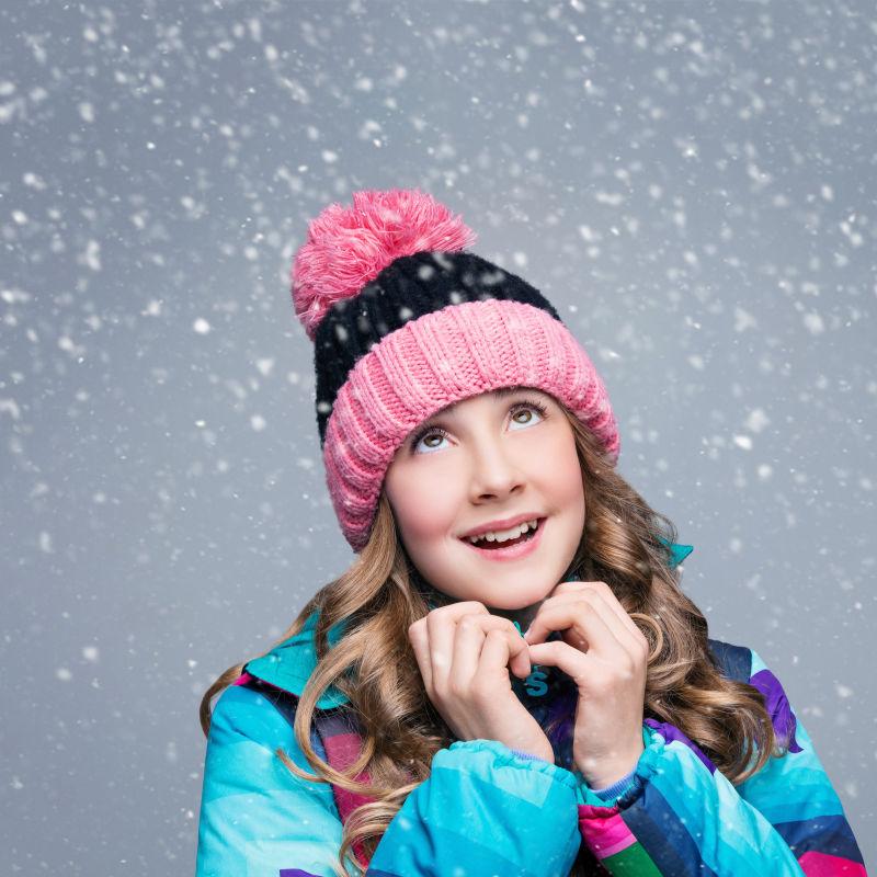 雪中戴着帽子的快乐的卷发小女孩