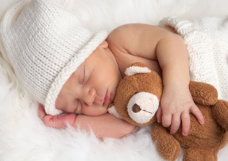 新生的婴儿带着白色帽子抱着小熊睡觉